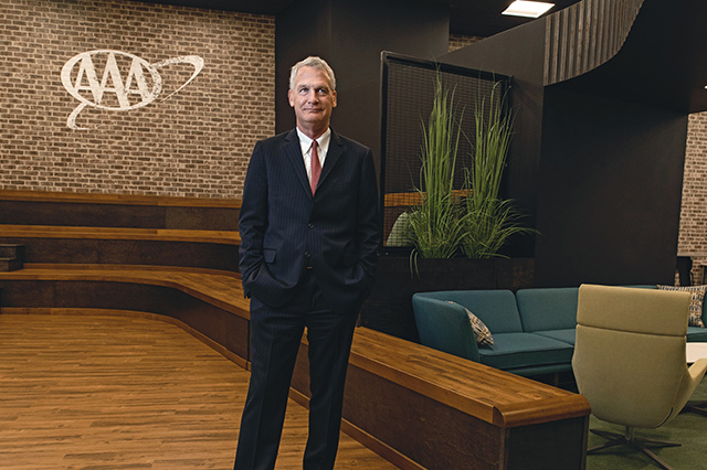 John Galvin in suit standing in front of AAA logo