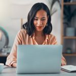 Woman working on laptop online, checking emails and planning on the internet while sitting in an office alone at work. Business woman, corporate professional or manager searching the internet