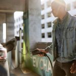 Man in denim jacket holding electric plug by car at charging station