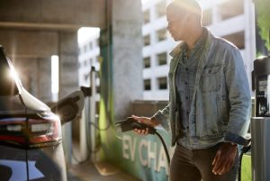 Man in denim jacket holding electric plug by car at charging station