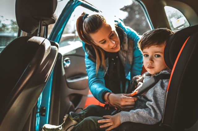 Happy Mother buckling her little son in car seat.